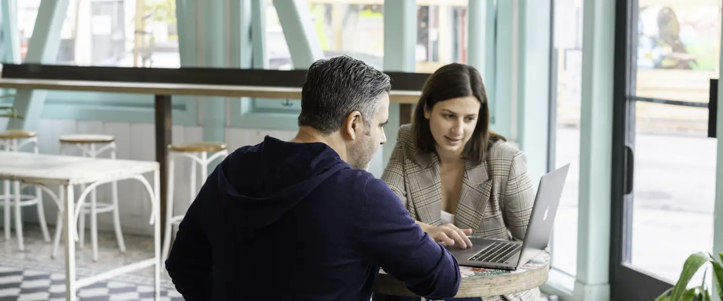 A sales rep and a business owner going over accounts on a laptop in a café