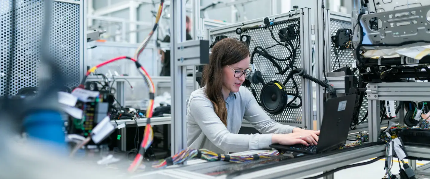 An engineer working on a laptop beside factory machinery