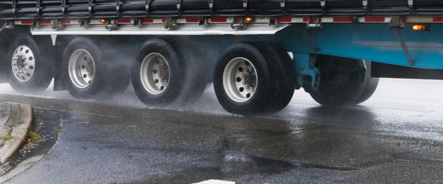 A semi truck's trailer wheels spraying water on a wet road