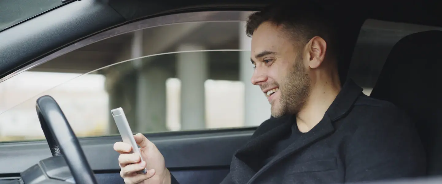 A sales rep smiling at his phone in the driver's seat